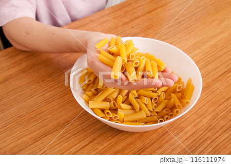 Uncooked raw healthy and pasta macaroni hand held by a Caucasian man, on wooden table in porcelain plate 116111974
