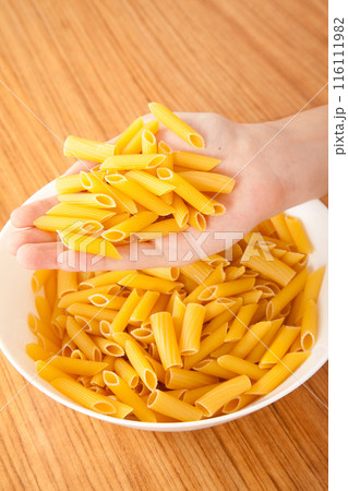 Uncooked raw healthy and pasta macaroni hand held by a Caucasian man, on wooden table in porcelain plate 116111982