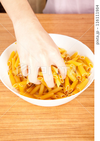Uncooked raw healthy and pasta macaroni hand held by a Caucasian man, on wooden table in porcelain plate Uncooked raw healthy and pasta macaroni hand held by a Caucasian man, on wooden table in porcelain plate 116111984