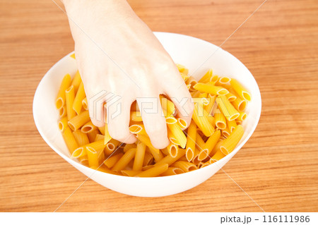 Uncooked raw healthy and pasta macaroni hand held by a Caucasian man, on wooden table in porcelain plate 116111986