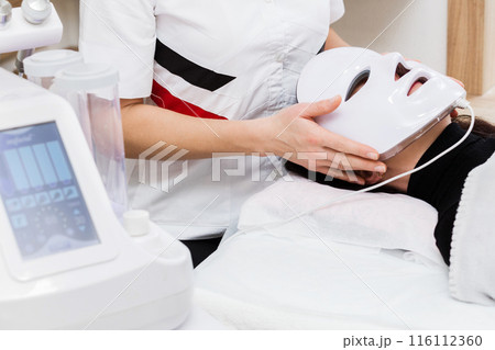 Cosmetologist Applying LED Mask for Facial Treatment 116112360