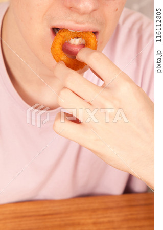 Caucasian man eats fresh onion rings with his hands, American fast food culture Caucasian man eats fresh onion rings with his hands, American fast food culture 116112805