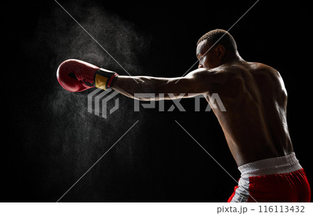 Jab punch. Muscular determined athlete in boxing gear practicing before fight, training with intensity isolated on black background Jab punch. Muscular determined athlete in boxing gear practicing before fight, training with intensity isolated on black background 116113432
