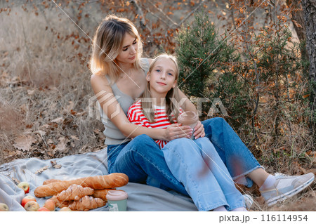 Mother sitting on plaid with her beautiful daughter outdoor in forest with sunshine. Mother sitting on plaid with her beautiful daughter outdoor in forest with sunshine. 116114954