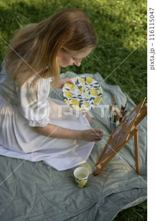 a beautiful young artist in a white dress paints a picture on the river bank a beautiful young artist in a white dress paints a picture on the river bank 116115047