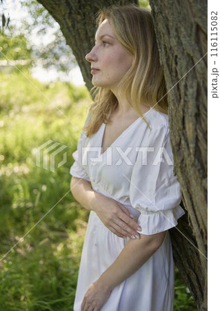 beautiful young artist in a white dress among the trees on the river bank 116115082