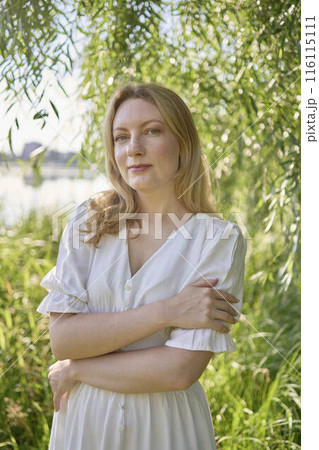 beautiful young artist in a white dress among the trees on the river bank 116115111