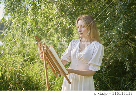 beautiful young artist in a white dress among the trees on the river bank 116115115