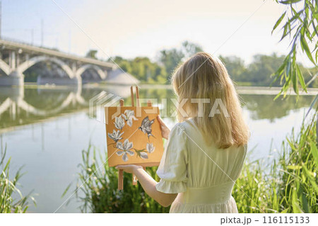 beautiful young artist in a white dress among the trees on the river bank 116115133