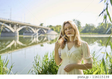 beautiful young artist in a white dress among the trees on the river bank 116115139