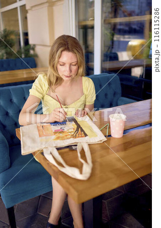 a beautiful young artist in a yellow dress paints a customized shopping bag a beautiful young artist in a yellow dress paints a customized shopping bag 116115286