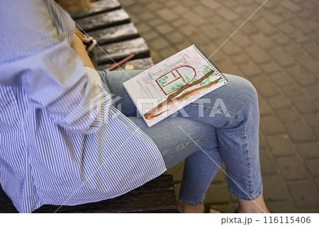a young artist draws a sketch of a window on the streets of the city 116115406