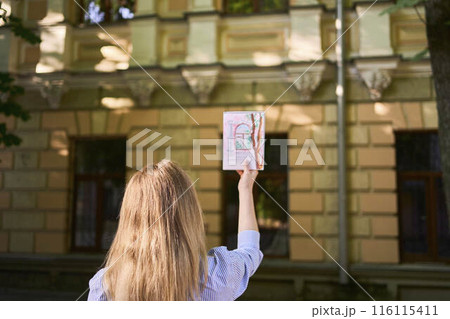 a young artist draws a sketch of a window on the streets of the city 116115411