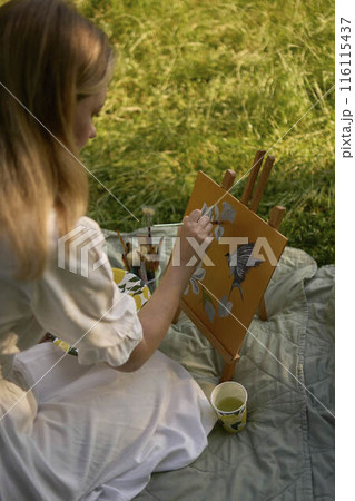 a beautiful young artist in a white dress paints a picture on the river bank a beautiful young artist in a white dress paints a picture on the river bank 116115437