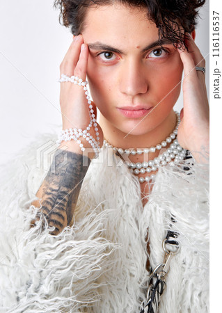 brunette male in fluffy coat and necklace looking at camera, touching temples brunette male in fluffy coat and necklace looking at camera, touching temples 116116537