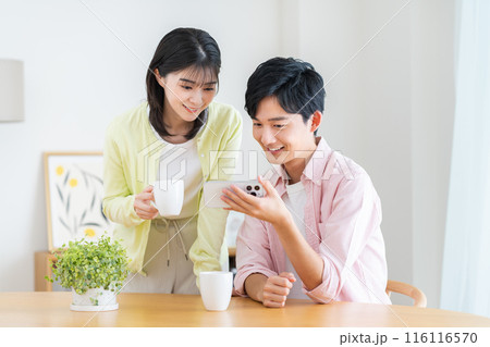 自宅でスマホを見る若い夫婦 116116570