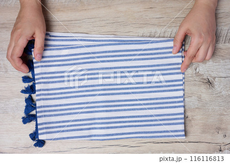 Two female hands hold a white and blue striped kitchen towel on the table, top view Two female hands hold a white and blue striped kitchen towel on the table, top view 116116813