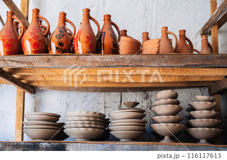Clay plates and hand-painted Uzbek ceramic jugs on shelf in a pottery workshop in Uzbekistan 116117613