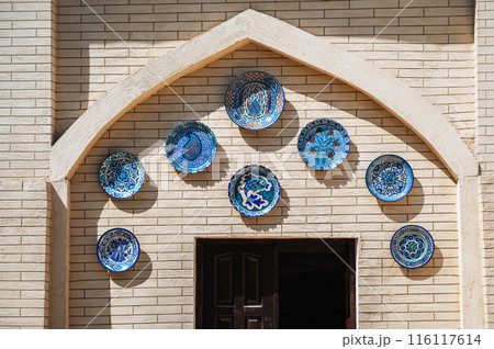 traditional oriental Uzbek ceramic plates hand-painted in Arabic style on wall of a pottery workshop 116117614
