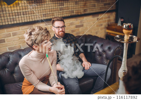 cheeerful ginger man is looking at blond girl who is smoking hookah 116117892