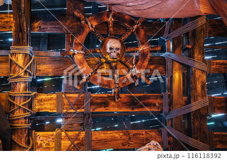 wooden steering wheel with a skull in captain's cabin on an medieval pirate ship 116118392