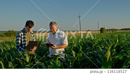 Two farmers working in a field, using a laptop and a tablet. Technology in agriculture Two farmers working in a field, using a laptop and a tablet. Technology in agriculture 116118527