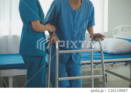 Physical therapist helps a male patient use a walker to practice walking. Support yourself from recovery from sore legs and ankles. Physical therapy service concept. Physical therapist helps a male patient use a walker to practice walking. Support yourself from recovery from sore legs and ankles. Physical therapy service concept. 116119067