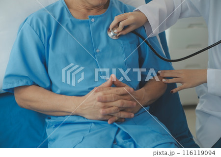 Doctor using stethoscope to listen senior man heart during examination in hospital room and wearing visor as safety precaution against coronavirus. Medical control for infections, disease. Doctor using stethoscope to listen senior man heart during examination in hospital room and wearing visor as safety precaution against coronavirus. Medical control for infections, disease. 116119094