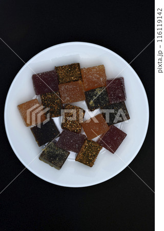 Multicolored marmalade on a white plate. Sweets on a black background. 116119142