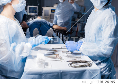 Surgical tools lying on table with nurse near and surgeons at background. Surgical tools lying on table with nurse near and surgeons at background. 116120195