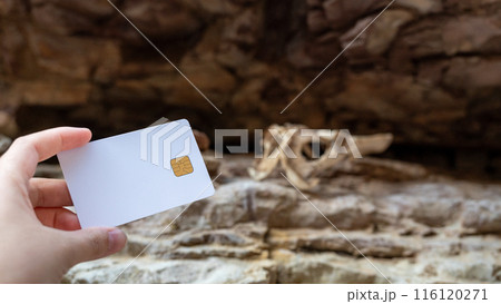 A woman's hand holds a white bank card against a background of a rocky canyon and an animal skull. A woman's hand holds a white bank card against a background of a rocky canyon and an animal skull. 116120271