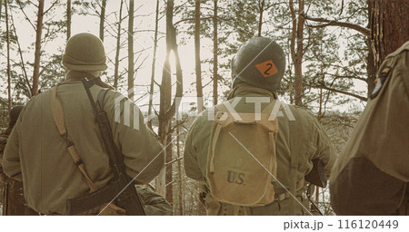 Back View On American Infantry Soldier Watch For Bright Sun At Winter Day. Group Of Usa Soldiers Armed Of Assault Rifle. Usa Army Soldiers Of World War Ii Back View On American Infantry Soldier Watch For Bright Sun At Winter Day. Group Of Usa Soldiers Armed Of Assault Rifle. Usa Army Soldiers Of World War Ii 116120449