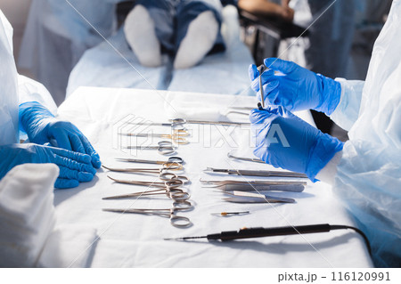 Surgical tools lying on table with nurse near and surgeons at background. 116120991