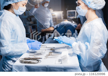 Surgical tools lying on table with nurse near and surgeons at background. 116120996