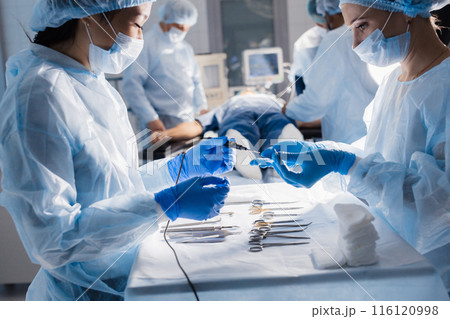 Surgical tools lying on table with nurse near and surgeons at background. 116120998