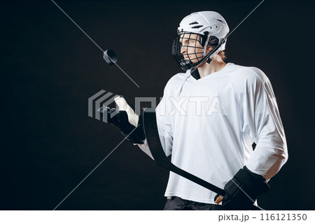 Portrait of ice-hockey player with hockey stick and puck isolated over black 116121350