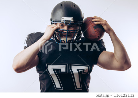 Muscular american football player in protective uniform and helmet holding ball 116122112