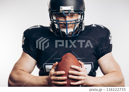 Muscular american football player in protective uniform and helmet holding ball Muscular american football player in protective uniform and helmet holding ball 116122735