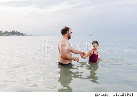 side view of father standing in the water together with his daughter side view of father standing in the water together with his daughter 116122911