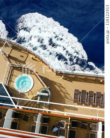 A fragment of the plank deck of a luxury cruise ship with brown sun loungers and a round jacuzzi A fragment of the plank deck of a luxury cruise ship with brown sun loungers and a round jacuzzi 116122913