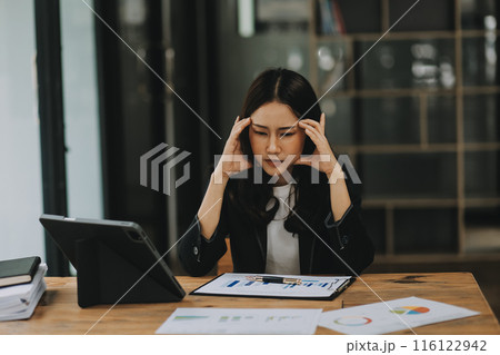 Young sad businesswoman is sitting at table, covering his face On desk is laptop, tablet computer, Stress. Serious woman concentrating on his paper work. 116122942