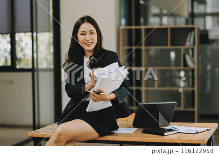 Asian businesswoman talking on phone, using laptop, looking at screen, entrepreneur manager consulting client by call, looking at computer screen, discussing project, reading information 116122958