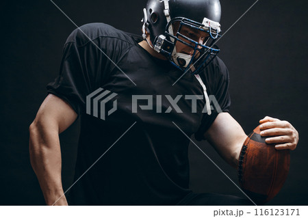 American football player in black sportwear with a ball on black background American football player in black sportwear with a ball on black background 116123171