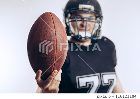 Muscular american football player in protective uniform and helmet holding ball Muscular american football player in protective uniform and helmet holding ball 116123184