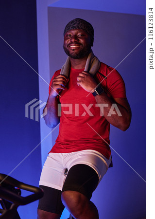 African American man resting after cardio train and holding his gray towel to wipe sweat, he smiling widely and sincerely showing his teeth 116123814