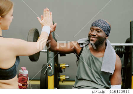 African American man sitting on bench and high fiving his sporty and active gym crush 116123912