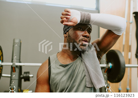 Young African American sportsman wiping off sweat and feeling delayed onset muscle soreness after workout 116123923