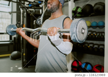Medium close up of African American man picking up ten kilogram barbell Medium close up of African American man picking up ten kilogram barbell 116123969