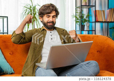 Amazed young man use laptop computer, receive good news message, shocked by victory, celebrate win 116124378