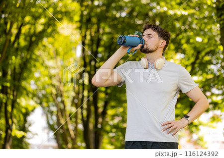 Sporty athletic thirsty man runner jogger drinking water after sport workout in park outdoors Sporty athletic thirsty man runner jogger drinking water after sport workout in park outdoors 116124392